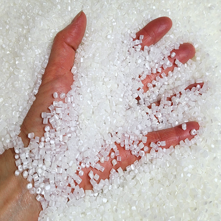 A hand holding and covered with translucent white plastic pellets or granules, photographed close-up against more of the same material.