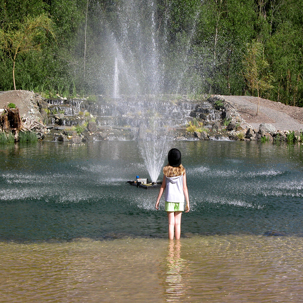 Little girl standing in a large swimming pond with waterfalls and a lake fountain