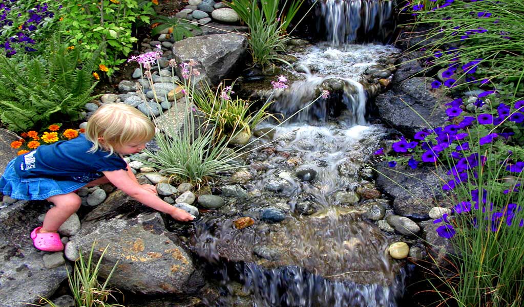 Child playing in a beautiful pondless waterfall created using a Russell Watergardens Ultimate Pondless Waterfall Kit