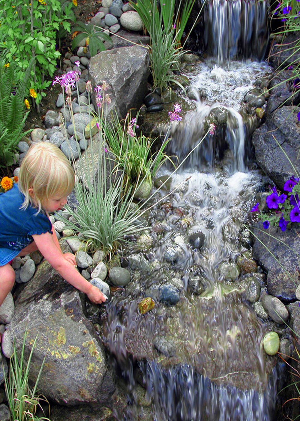 Three stepped waterfalls cascading over boulders with a child placing stones in the stream