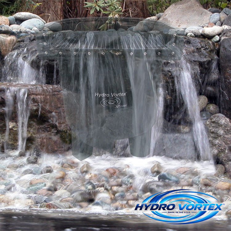 A Hydro Vortex water feature filter or waterfall panel installed in a rocky outdoor stream setting, with flowing water around it and a brand logo overlay in the bottom right corner.