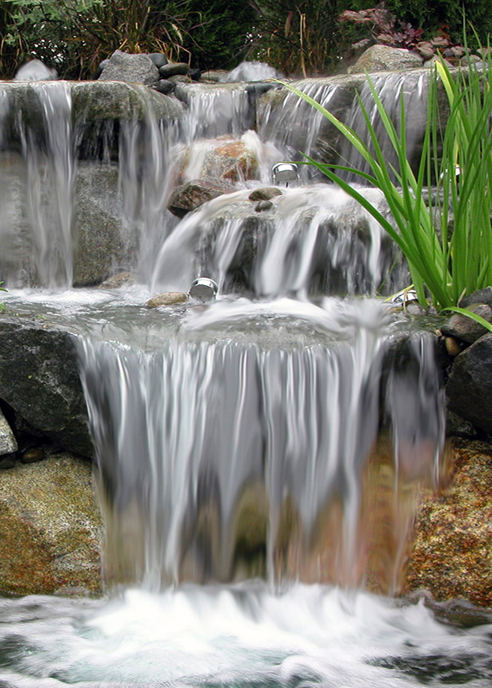Beautiful four step waterfalls over boulders into a pond - built by Russell Watergardens
